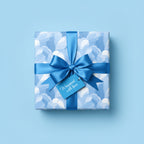 Square gift box wrapped in blue floral wrapping paper with satin bow and "Wrapped with love" tag.