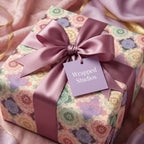 Luxury floral wrapping paper with a mauve satin bow and Wrapped Studios tag on an elegant gift box.