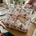 Boho botanical wrapping paper by Wrapped Studios on a gift box with pink twine and an 'Enjoy' tag.