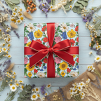 Square gift box in colorful floral wrapping paper with red ribbon, surrounded by dried flowers.