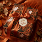 Vintage Halloween wrapping paper with ghosts and pumpkins, tied with an orange ribbon by Wrapped Studios.