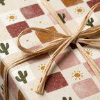 Boho cactus and sun wrapping paper with terracotta checkered print and raffia bow by Wrapped Studios.