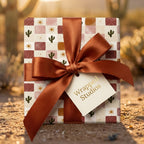 Boho cactus wrapping paper with a terracotta satin bow in a desert setting by Wrapped Studios.