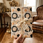 Hand holding a gift wrapped in vintage celestial sun and moon wrapping paper by Wrapped Studios.