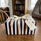 Elegant navy and burgundy striped wrapping paper by Wrapped Studios, featuring a cream satin bow and gift tag.