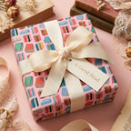 Book lover wrapping paper with cream ribbon and 'A Good Read' tag on a pink box. Wrapped Studios.