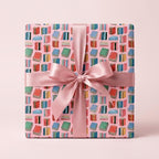 Whimsical book wrapping paper on a gift box with a pink satin bow, book lover gift wrap by Wrapped Studios.