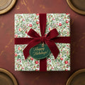 Square gift wrapped in floral Christmas wrapping paper with a red velvet bow and "Happy Holidays!" tag.
