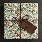 Square gift wrapped in floral Christmas wrapping paper with red berries and tied with a brown suede ribbon.