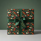Elegant square gift wrapped in dark floral Christmas wrapping paper with green ribbon and berry design.