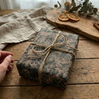 Elegant floral gift wrapped in botanical wrapping paper with a jute bow on rustic wood.