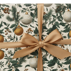 Elegant Christmas gift wrap with vintage botanical holly, pine, and white/gold ornaments, tied with a sophisticated gold ribbon.