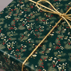 Close-up of a gift wrapped in dark green Christmas wrapping paper with a gold rope bow.