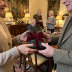 Couple exchanging a gift in luxury Christmas wrapping paper with a red velvet bow, by Wrapped Studios.