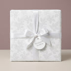 White floral wrapping paper with satin ribbon and gift tag by Wrapped Studios, ideal for elegant wedding gifts.