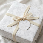 Elegant white floral wrapping paper with a cream velvet bow and holiday gift tag by Wrapped Studios.