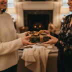 Two women exchanging a gift wrapped in elegant floral wrapping paper with a gold ribbon.