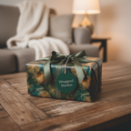Elegant gift wrapped in festive gold and green patterned wrapping paper with a satin ribbon on a wooden table.