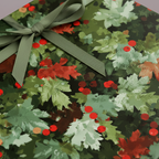 Elegant Christmas wrapping paper featuring a green ribbon and a festive leaf and berry pattern.
