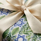 Hanukkah wrapping paper with blue Stars of David, green leaves, and cream bow by Wrapped Studios.