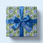 Modern Star of David Hanukkah wrapping paper with botanical leaves and a blue bow by Wrapped Studios.