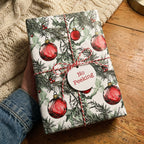 Christmas gift wrapped in festive ornament pattern paper with red baker's twine and "No Peeking" tag.