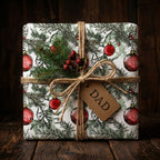 Wrapped Christmas gift for Dad with festive ornament pattern, natural twine bow, and sprig of greenery on rustic wood.