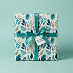 Modern botanical gift wrap in shades of teal, blue, and gold with a teal satin ribbon and white gift tag.