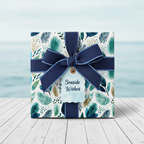 Coastal botanical wrapping paper with a navy ribbon, bow, and "Seaside Wishes" tag, perfect for summer or beach-themed gifts.