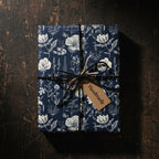 Elegant floral wrapping paper in navy and cream, tied with rustic twine and a "Handmade" tag, on a wood surface.