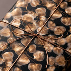 Elegant black and gold botanical wrapping paper with a copper wire bow, luxury gift wrap by Wrapped Studios.