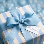Blue striped luxury wrapping paper with matching bow and gift tag by Wrapped Studios, ideal for baby showers.