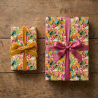 Colorful botanical floral wrapping paper on gifts with pink and gold ribbons on wood, by Wrapped Studios.