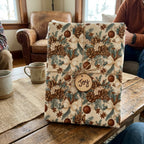 Rustic pinecone Christmas wrapping paper with a 'Joy' tag on a cozy wooden table by Wrapped Studios.