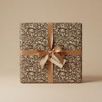 Elegant gift wrapped in floral wrapping paper with gold ribbon and "With Care" tag.