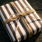Rustic brown and white striped wrapping paper with a twine bow on a wooden table by Wrapped Studios.
