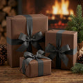 Three coffee brown gift boxes with black ribbons in front of a fireplace and Christmas tree.