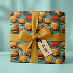 Square gift wrapped in fun, quirky burger pattern wrapping paper with a gold ribbon.
