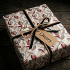 Elegant floral gift wrap with burgundy leaves, black velvet ribbon, and Cheers tag by Wrapped Studios.