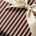 Striped wrapping paper in burgundy and cream with a silky champagne-colored ribbon and bow.