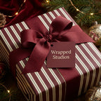 Elegant striped Christmas gift wrap with burgundy ribbon and tag on a decorated holiday table.