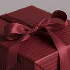 Burgundy striped wrapping paper with satin ribbon tied on a square gift box.