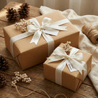 Two rustic-chic gifts wrapped in solid brown paper with white satin ribbon & berry accents, on a wood table.