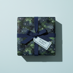 Square gift wrapped in starry camo print paper with navy ribbon and tag.