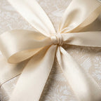 Elegant beige floral wrapping paper with an ivory satin bow, luxury wedding gift wrap by Wrapped Studios.