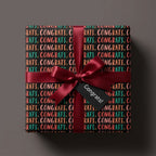 Graduation wrapping paper with colorful congrats print, burgundy ribbon, and gift tag by Wrapped Studios.