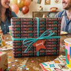 Congratulations wrapping paper with colorful text and a teal bow at a party by Wrapped Studios.