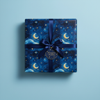 Square gift wrapped in navy celestial wrapping paper with moons, stars, and navy ribbon.