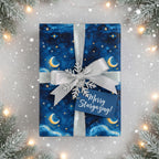 Navy blue Christmas gift wrap with moon & star pattern, silver ribbon, and "Merry Stargazing" tag.