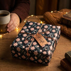 Starry celestial wrapping paper in navy and rose gold on a cozy Christmas gift by Wrapped Studios.